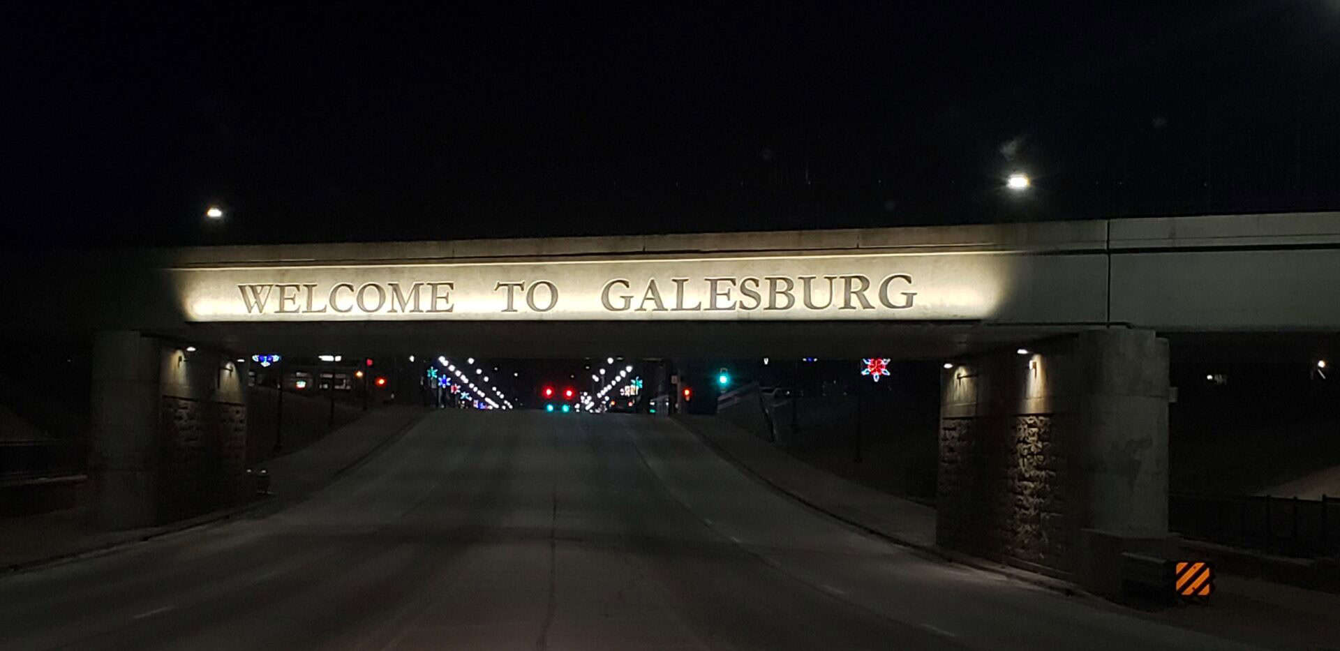 Welcome to Galesburg bridge sign illuminated at night with downtown lights in the background