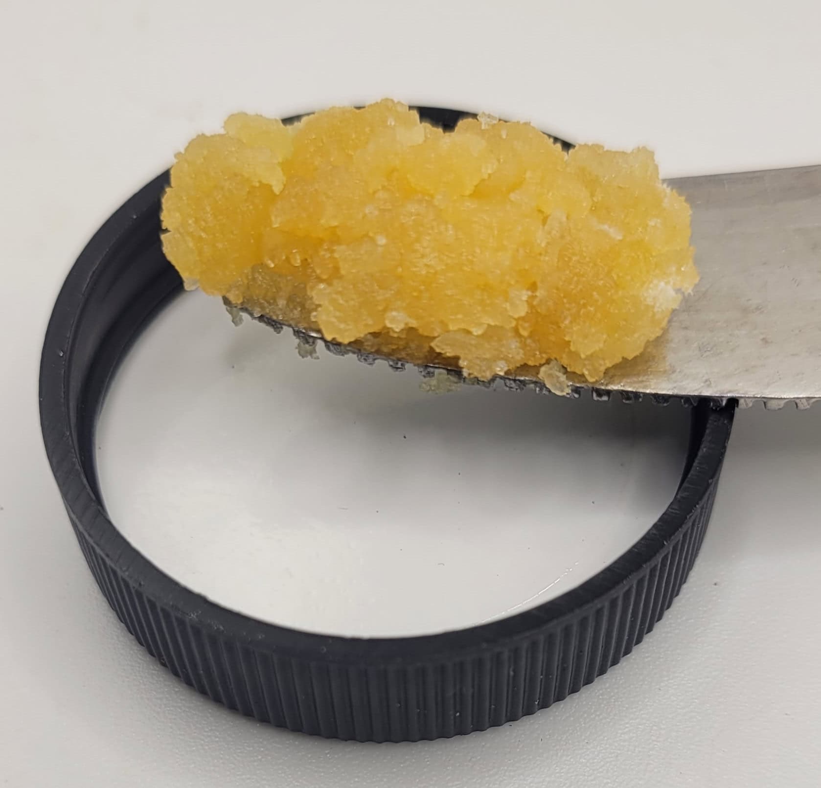 Yellow substance on metal spoon, black lid base