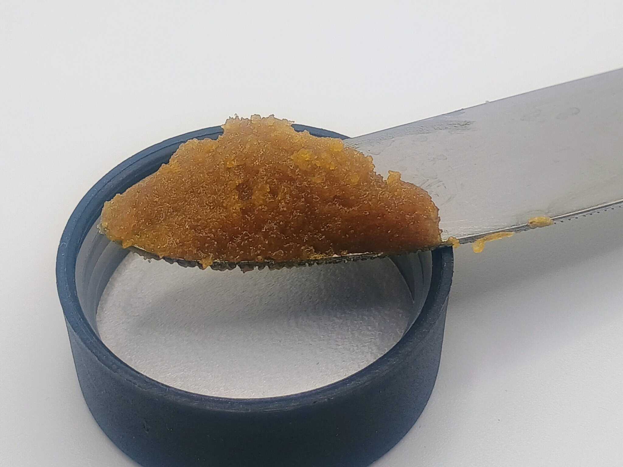 Knife spreading brown paste from jar onto white surface