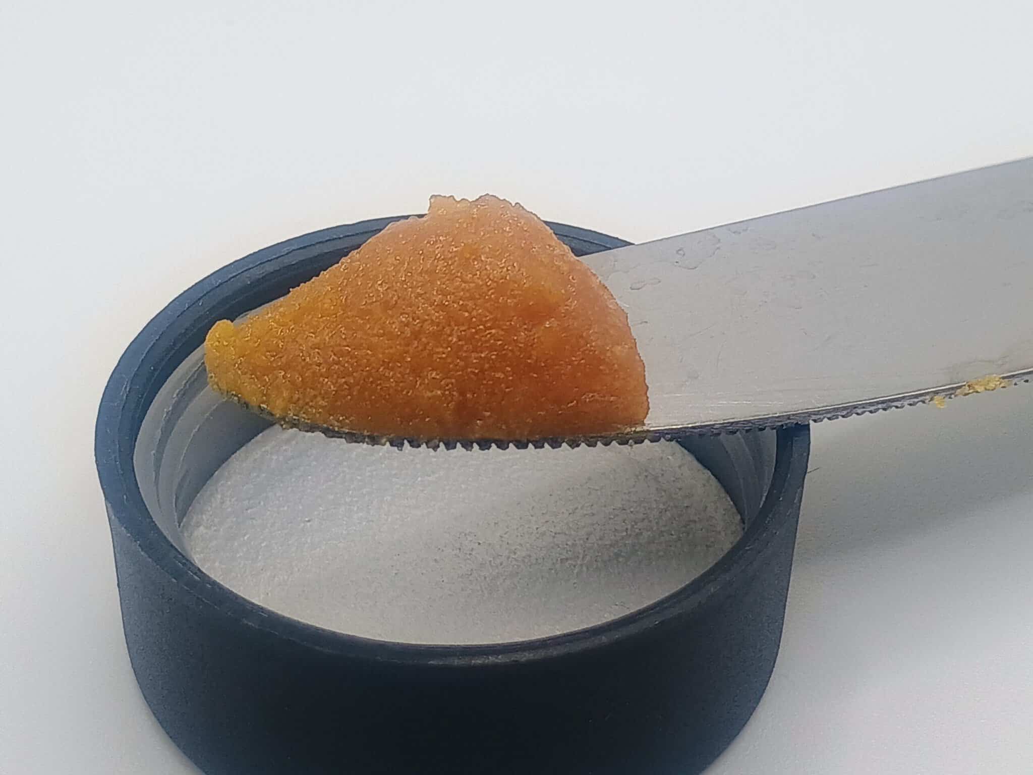 Knife spreading orange paste on container lid.