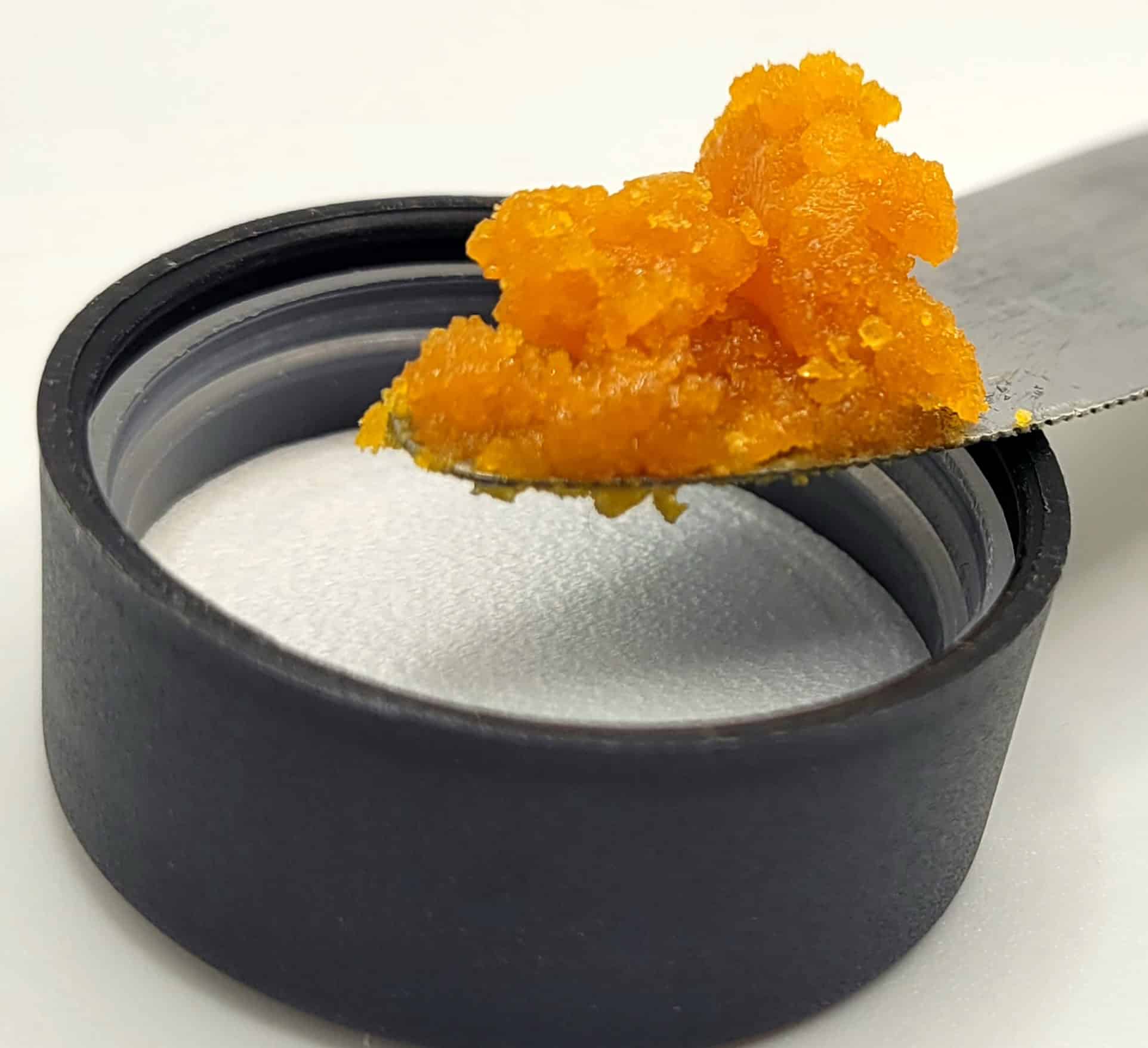 Knife with orange substance on black lid.