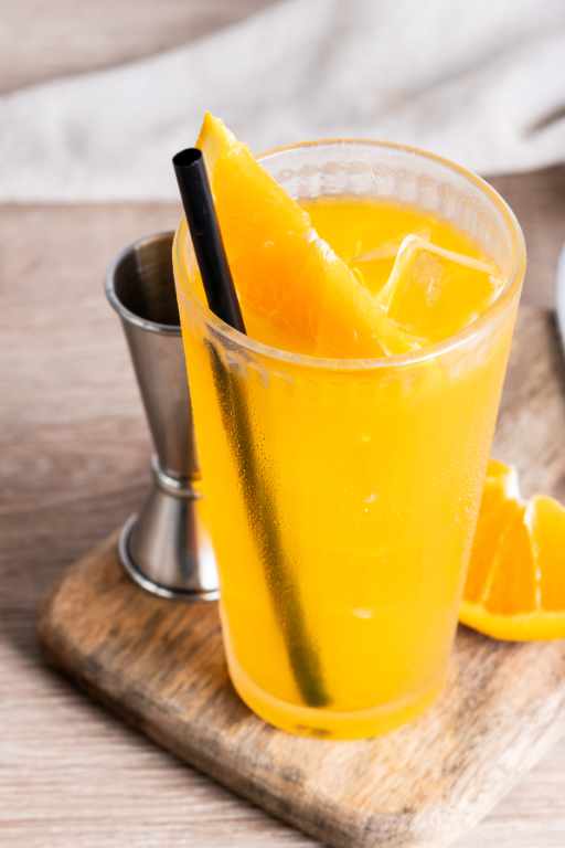 Chilled orange juice with straw and citrus slice.