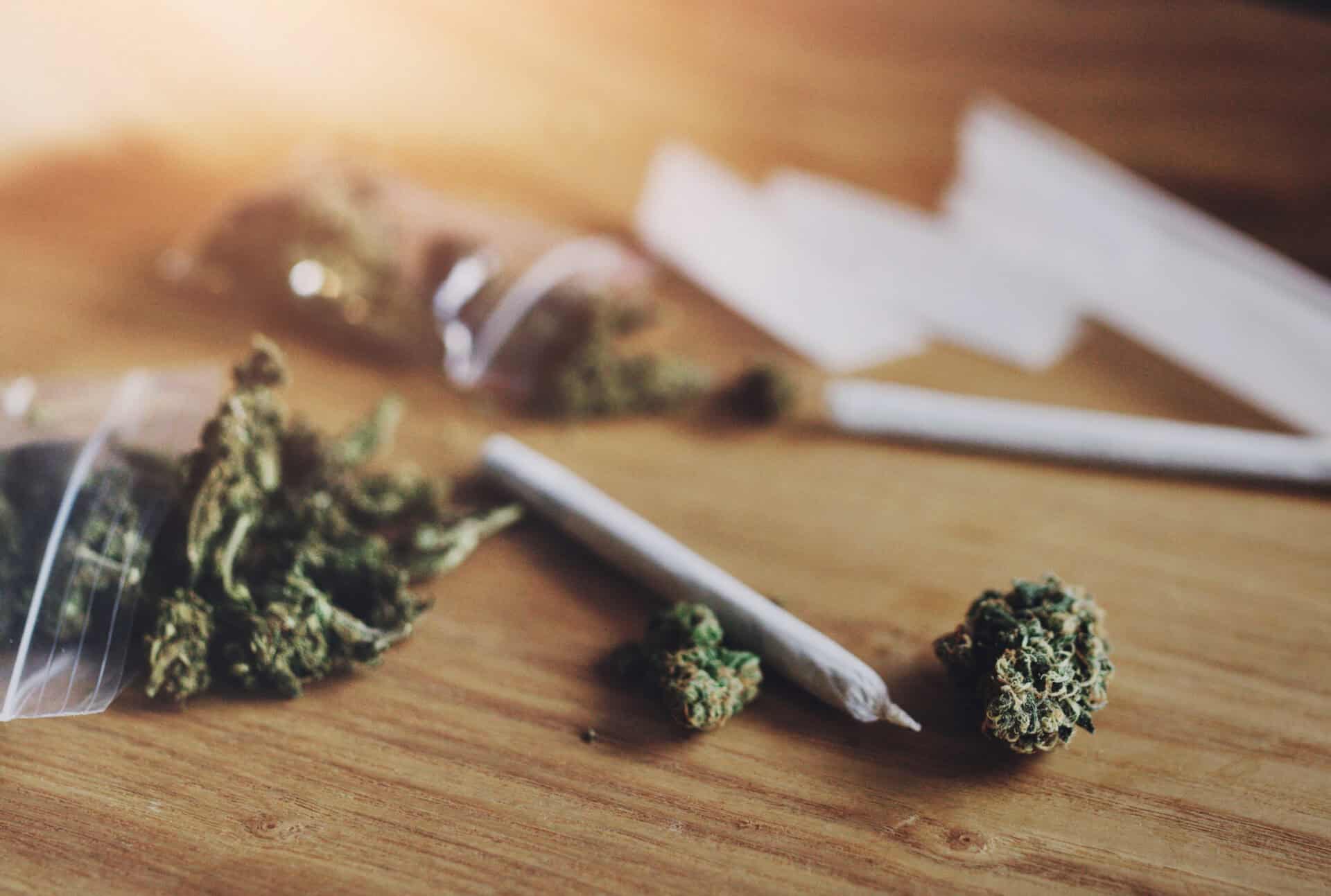 Cannabis buds and rolled joint on wooden surface.